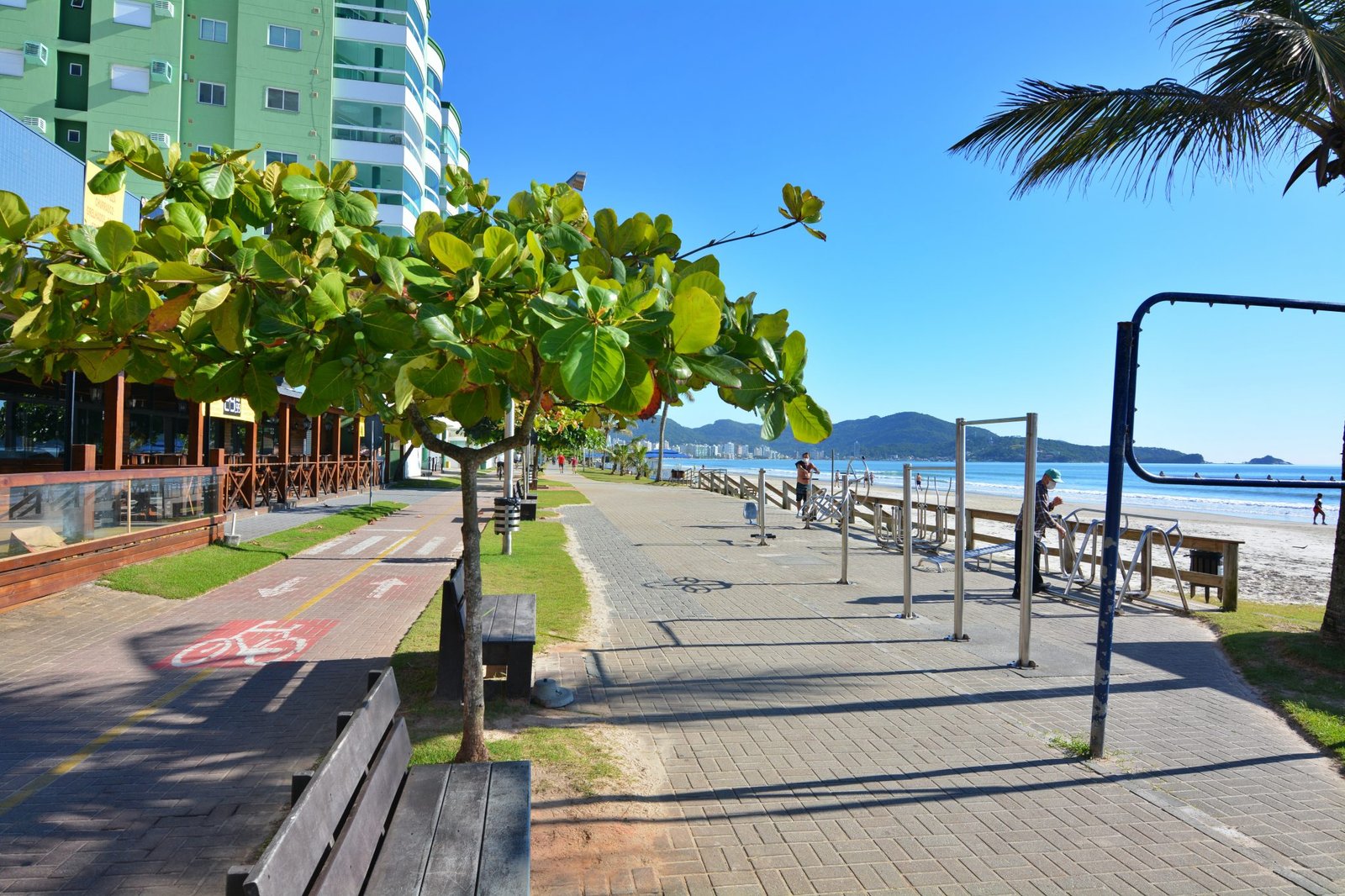 Foto da paisagem da cidade de Itapema contendo a orla do centro, contando com o pier, cliclovia arvores e o mar ao fundo.